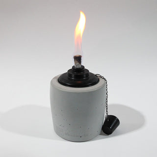 Gartenfackel in Grau mit 13cm Durchmesser und 19cm Hoch. Der schwarze Einsatz des Ölbrenners erzeugt eine schöne gleichmäßige Flame. Der Löschdeckel hängt an einer feinen Kette auf der rechten Seite herunter. 