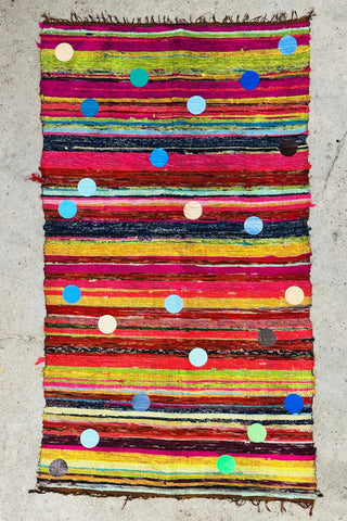 Rechteckiger Stoffteppich ca. 180 × 105 cm aus recyceltem Material mit großem, buntem handbedruckten „BALLS“-Design, flach liegend in einem modernen Wohnraum inszeniert.
