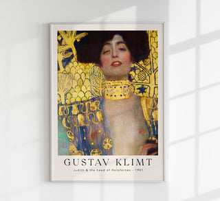 Exhibition-Poster zu Gustav Klimts „Judith and the Head of Holofernes“ mit naher Ansicht der vergoldeten Halbfigur Judiths, dekorativem Goldgrund und typografischem Ausstellungstitel, als Fine-Art-Print gerahmt in einem modernen Wohnzimmer mit dunkler Wand und akzentuierter Beleuchtung
