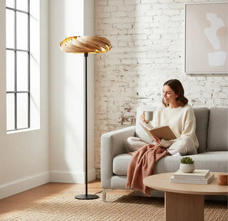 Gofurnit Veneria floor lamp with a swirling, layered amberwood shade and a black metal stand against a white brick wall.