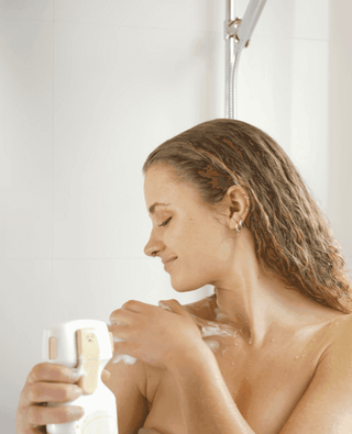 Blonde Frau duscht begeistert mit YOUCISION Dispenser und schäumt ihre Schulter unter der Dusche ein