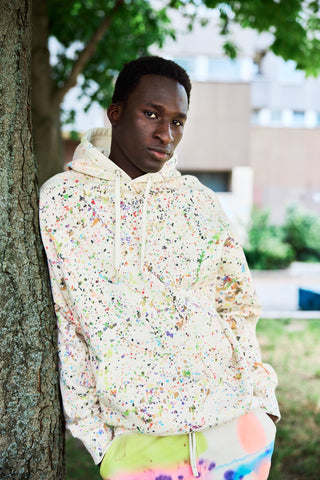 Schwerer Unisex-Hoodie aus Bio-Baumwolle mit bunter, handbemalter Drip-Optik im Pollock-Stil, frontal fotografiert, lockere Passform vor neutralem Hintergrund.
