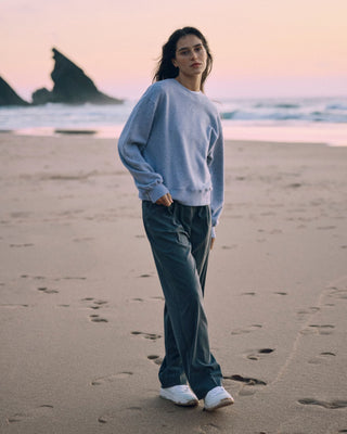 Graue Classic Hose für Damen aus zertifizierter Wolle mit Bundfalten, kombiniert mit hellgrauem Sweater, getragen am Strand bei Sonnenuntergang.