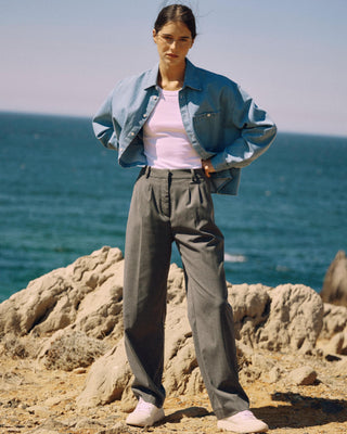 Graue Classic Hose für Damen aus zertifizierter Wolle mit Bundfalten, getragen vor Felsen und Meer.