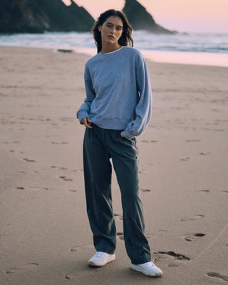 Graue Classic Hose für Damen aus zertifizierter Wolle, kombiniert mit hellgrauem Sweater, getragen am Strand in der Dämmerung.