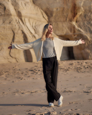 Schwarze Classic Hose für Damen aus zertifizierter Wolle, getragen am Strand mit gestreiftem Shirt und heller Strickjacke.