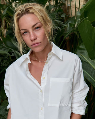 Kurze Damen Hemdbluse in Weiß aus Bio-Baumwolle von WOTE, frontal am Model getragen, Editorial Aufnahme vor grünen Pflanzen.