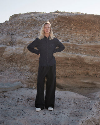 Model trägt ein dunkles, weiches Oversized Denimhemd aus Bio-Baumwolle vor einer hellen Felslandschaft.