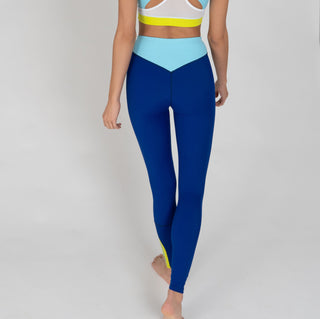 Eine Frau trägt eine dunkelblaue Sportleggings mit einem hellblauen Bund und einem gelben Akzentstreifen mit Bodyguard-Logoam Bein unten