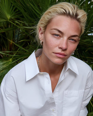 Kurze Damen Hemdbluse in Weiß aus Bio-Baumwolle, Nahaufnahme am Model vor dichtem grünen Palmenhintergrund.