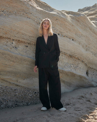 Schwarze Marlene Hose für Damen aus zertifizierter Wolle, kombiniert mit Blazer, getragen vor heller Felswand.