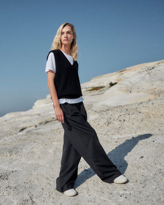 Schwarze Marlene Hose für Damen aus zertifizierter Wolle, kombiniert mit weißem T-Shirt und schwarzem Stricktop, getragen in heller Felslandschaft.
