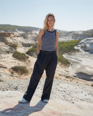 Schwarze Marlene Hose für Damen aus zertifizierter Wolle, kombiniert mit schwarz-weiß gestreiftem Top, getragen in sonniger Küstenlandschaft.
