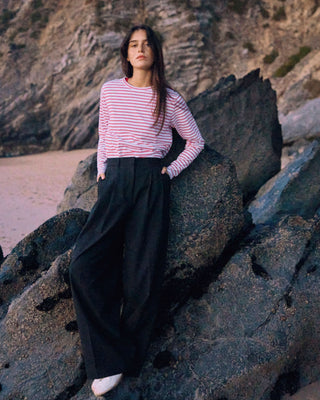 Schwarze Marlene Hose für Damen aus zertifizierter Wolle mit rot-weiß gestreiftem Longsleeve, angelehnt an dunkle Felsen am Strand.