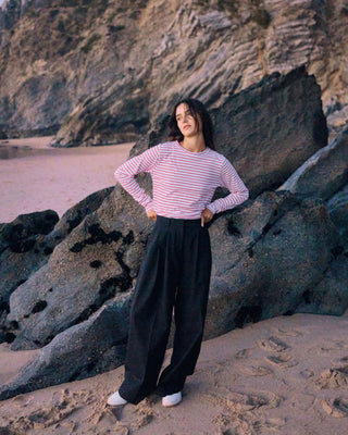 Schwarze Marlene Hose für Damen aus zertifizierter Wolle mit rot-weiß gestreiftem Longsleeve vor dunklen Felsen am Strand.
