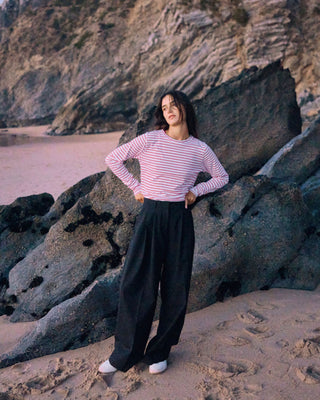 Schwarze Marlene Hose für Damen aus zertifizierter Wolle mit rot-weiß gestreiftem Longsleeve vor dunklen Felsen am Strand.