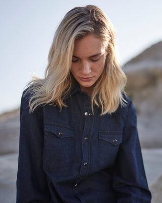 Model trägt ein dunkelblaues Oversized Denim Hemd aus Bio-Baumwolle mit Druckknöpfen, frontal aufgenommen in natürlicher Umgebung.