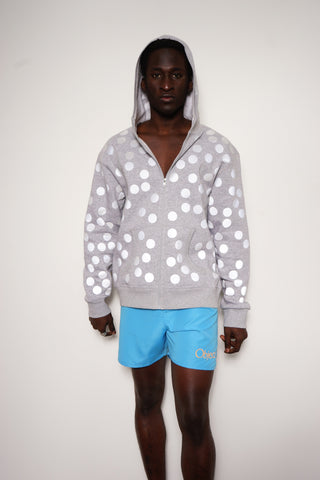 Unisex Zip-Jacke mit Kapuze und zwei Taschen, komplett mit matt-grauen, bei Licht stark reflektierenden Punkten bedruckt, frontal vor neutralem Hintergrund fotografiert.
