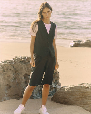 Model trägt eine schwarze Bermuda aus zertifizierter Wolle in frontaler Ansicht am Strand.