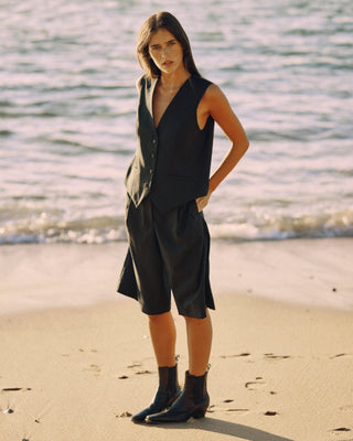 Model trägt eine schwarze Bermuda aus zertifizierter Wolle in einer Ganzkörperansicht am Strand.