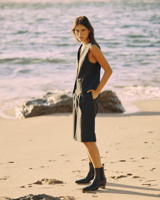 Model trägt eine schwarze Bermuda aus zertifizierter Wolle in seitlicher Ansicht am Strand.