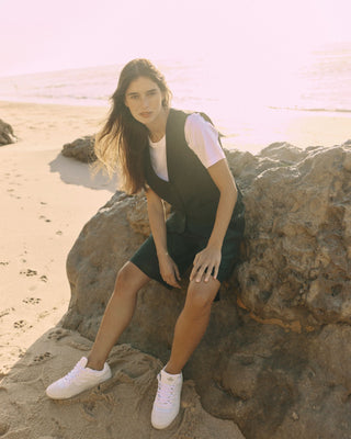 Model trägt eine schwarze Bermuda aus zertifizierter Wolle, sitzend auf einem Felsen am Strand.