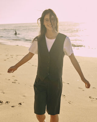 Model trägt eine schwarze Bermuda aus zertifizierter Wolle, gehend am sonnigen Strand.