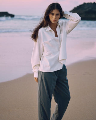 Offwhitefarbenes Cord Hemd für Damen aus Bio-Baumwolle mit lockerem Schnitt, getragen in ruhiger Ganzkörperansicht am Strand.