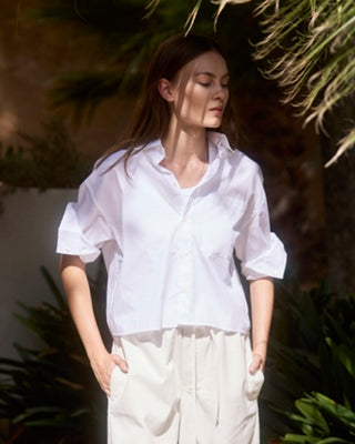 Kurze weiße Hemdbluse mit Brusttasche und hochgeschobenen Ärmeln, am Model mit heller Hose von vorn gezeigt.