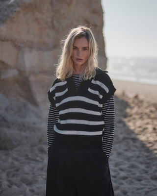 Schwarz-weiß gestreiftes Damen Longsleeve aus Bio-Baumwolle von WOTE, Frontansicht am Model mit Pullunder in natürlicher Strandumgebung.