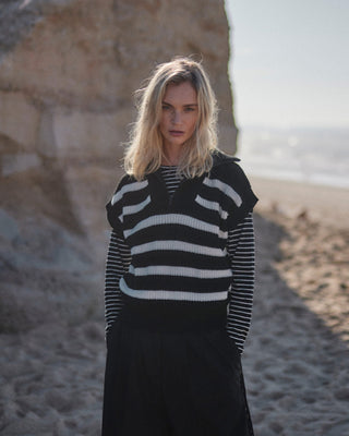 Schwarz-weiß gestreiftes Damen Longsleeve aus Bio-Baumwolle von WOTE, Frontansicht am Model mit Pullunder in natürlicher Strandumgebung.