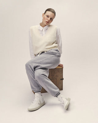 Offwhitefarbener Merino-Pullunder mit V-Ausschnitt, sitzend mit weißer Hemdbluse, grauer Hose und hellen Sneakern gezeigt
