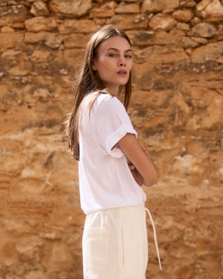 Weißes Relaxed-Fit Rundhals-T-Shirt aus Bio-Baumwolle für Damen, Rückenansicht an einem Model in sommerlicher Umgebung.