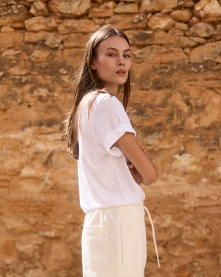 Weißes Relaxed-Fit Rundhals-T-Shirt aus Bio-Baumwolle für Damen, Rückenansicht an einem Model in sommerlicher Umgebung.