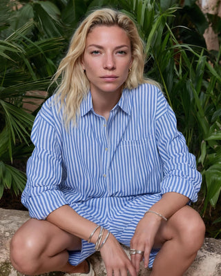 Blau-weiß gestreifte Damen Shorts aus Bio-Baumwolle von WOTE, getragen von einem Model im sitzenden Outdoor-Setting, kombiniert mit passendem Streifenhemd.