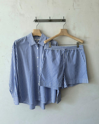 Blau-weiß gestreifte Damen Shorts aus Bio-Baumwolle von WOTE, zusammen mit passendem Streifenhemd auf Kleiderbügeln aufgehängt.