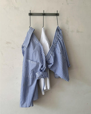 Blau-weiß gestreifte Damen Shorts aus Bio-Baumwolle von WOTE, kombiniert mit passendem Streifenhemd und weißem Top, gemeinsam an Wandhaken aufgehängt.