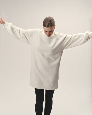 Oversized Damen Sweatkleid in Creme aus Bio-Baumwolle von WOTE, Ganzkörperansicht mit ausgestreckten Armen im Studio.