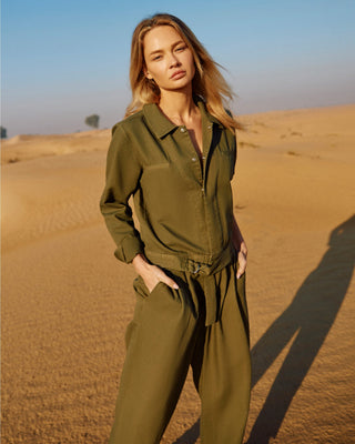 Olivfarbener Damen Utility Overall aus Bio-Baumwolle von WOTE, getragen von einem Model im Outdoor-Setting, mit Taillenband und Canvas-Struktur.