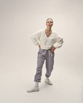 Sweatshirt in Offwhite mit V-Ausschnitt und lockerem Sitz, stehend zu grauer Hose gezeigt
