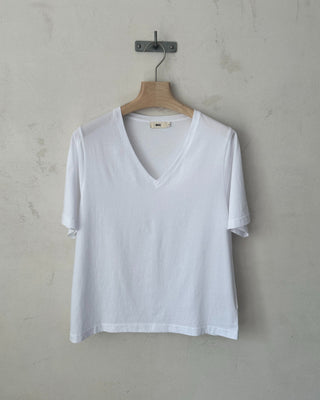 Weißes Damen-T-Shirt mit V-Ausschnitt, kurzen Ärmeln und lockerem Schnitt, frontal auf einem Holzbügel.