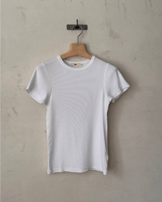 Weißes geripptes Damen T-Shirt aus Bio-Baumwolle auf Holzbügel vor heller Wand.