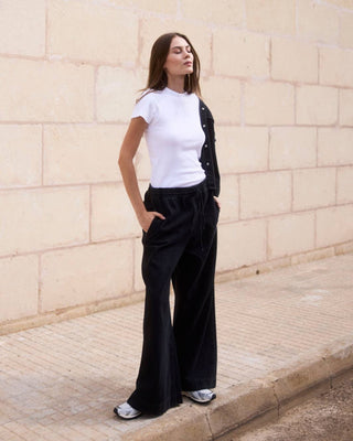 Modell trägt ein weißes geripptes T-Shirt aus Bio-Baumwolle im Ganzkörper-Look vor heller Steinwand.