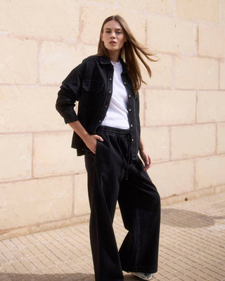 Modell trägt ein weißes geripptes T-Shirt aus Bio-Baumwolle im Ganzkörper-Look mit offener schwarzer Jacke.