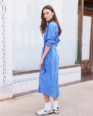 Seitenansicht eines einfarbig blauen Hemdblusenkleids für Damen in Midi-Länge aus Organic Cotton mit Bindegürtel, am Model getragen.