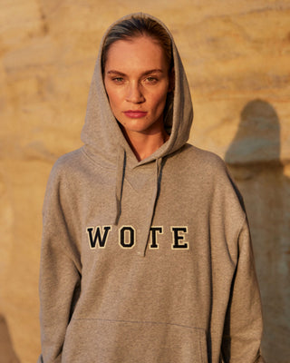 Damen WOTE Logo Hoodie in Grau Melange aus Organic Cotton, Frontansicht mit hochgezogener Kapuze im warmen Abendlicht
