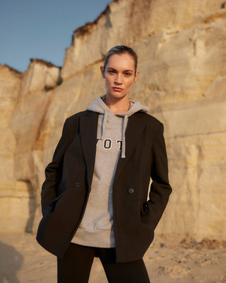 Damen WOTE Logo Hoodie in Grau Melange aus Organic Cotton, kombiniert mit schwarzem Blazer, Frontansicht im Abendlicht